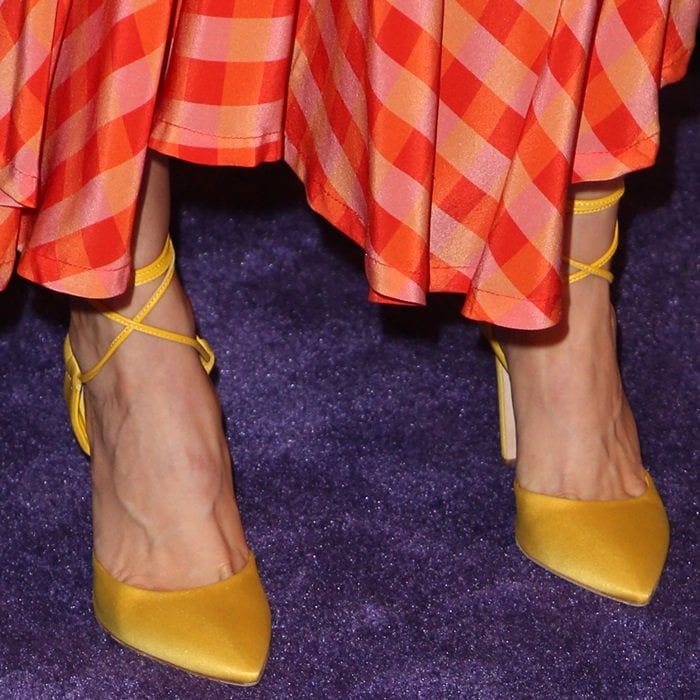 Alison Brie shows off her yellow satin Olgana Paris pumps with delicate wraparound ankle straps, adding a sharp pointed-toe finish to her gingham PaleyFest look