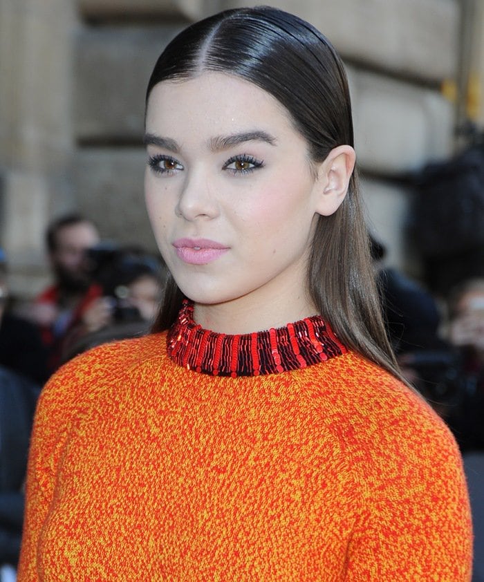 Hailee Steinfeld pairs her vibrant Dior look with sleek, center-parted hair and soft, luminous makeup at Paris Fashion Week