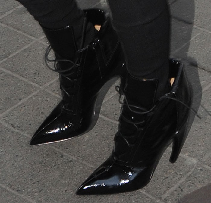 Kim Kardashian’s patent leather Givenchy lace-up ankle boots showcase sharply pointed toes and dramatic curved heels that elevate the sleek monochrome streetwear look
