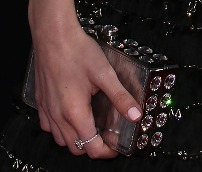 Kiernan Shipka carries a glittering Miu Miu stone-embellished hard-case clutch, paired with a delicate diamond ring for a refined finishing touch