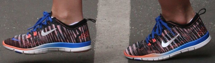 A close-up reveals her Nike Free 5.0 TR Fit 4 Print sneakers, featuring a multicolor knit upper, blue laces, and a flexible sole built for lightweight movement