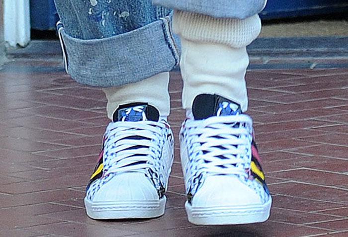 Rita Ora styled her vibrant Adidas “Super” Superstar sneakers with cuffed, paint-splattered jeans and thick cream socks, letting the bold comic-book graphics pop against her casual streetwear look