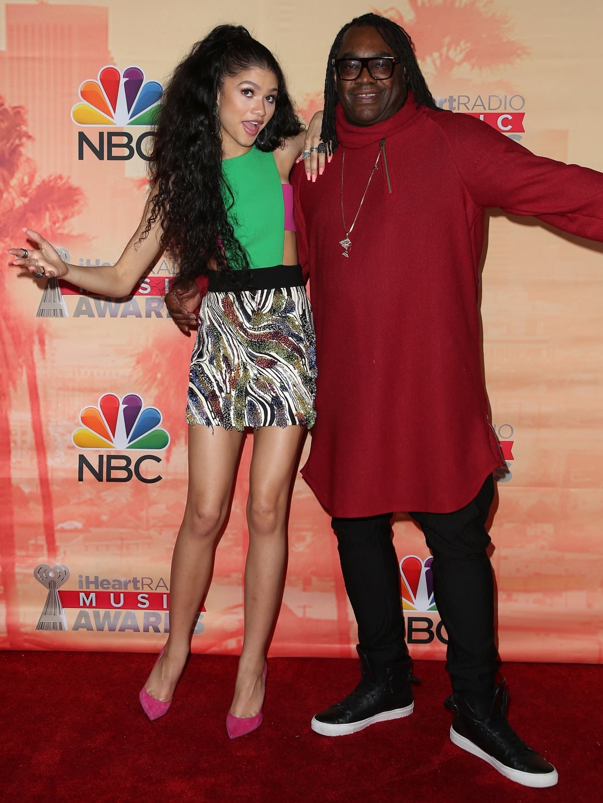 Zendaya lights up the 2015 iHeartRadio Music Awards red carpet in a bold Fausto Puglisi mini dress paired with hot-pink Jimmy Choo pumps, posing playfully alongside her father, Kazembe Ajamu Coleman