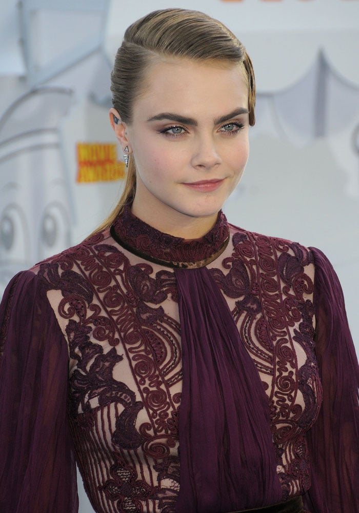 Cara Delevingne stuns in a richly embroidered eggplant Reem Acra mini dress, pairing its intricate lacework with sleek, sculpted hair and plum-toned glam