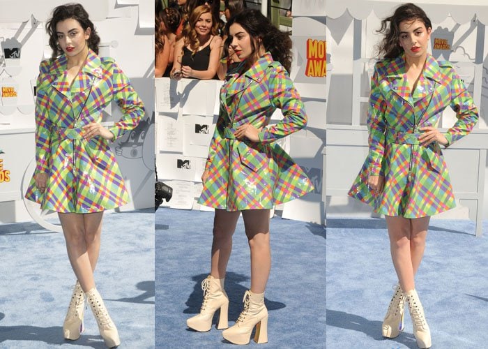 Charli XCX leaned fully into mid-2010s maximalism in a rainbow plaid Jeremy Scott patent trench coat, pairing the glossy mini dress with towering Vivienne Westwood platform boots that exaggerated the look’s playful punk attitude
