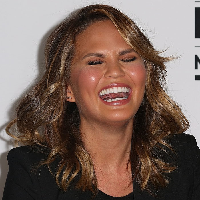 Chrissy Teigen lights up the room mid-conversation, her tailored black blazer and natural glam makeup underscoring her effortless approach to event dressing