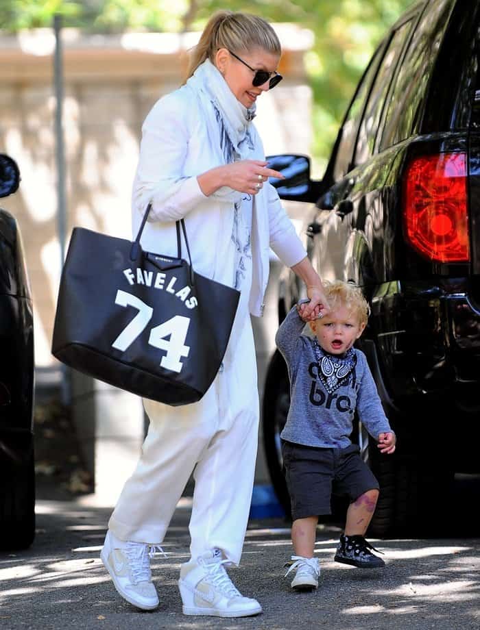 Fergie steps out in style wearing white drop-crotch joggers, wedge-heeled sneakers, and a Givenchy Favelas 74 tote while holding hands with her son, Axl