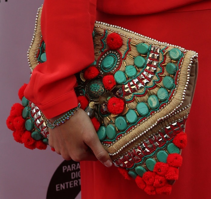 Jamie Chung accessorizes her red wrap dress with a vibrant, intricately designed clutch featuring turquoise stones and red pom-poms