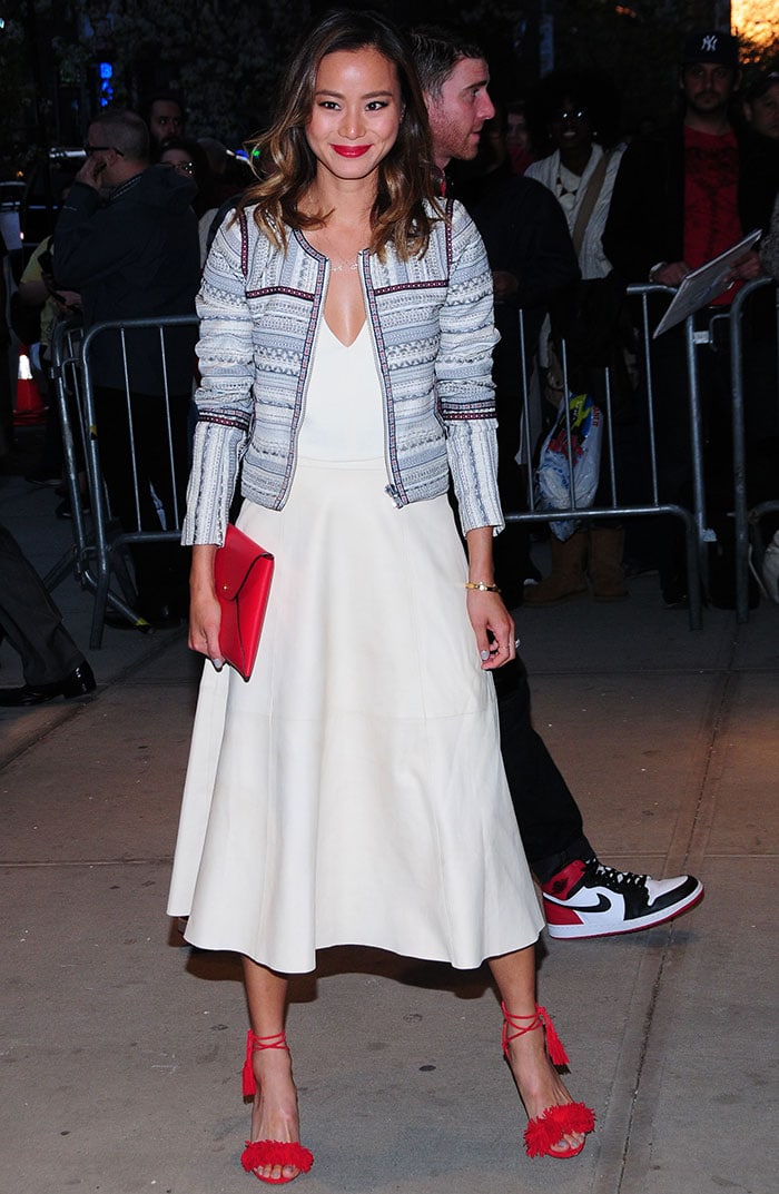 Jamie Chung lights up the red carpet in a Tularosa Griffin jacket layered over a white V-neck dress, styled with a bold Kate Spade Saturday clutch and Aquazzura’s poppy-red Wild Thing tasseled suede sandals