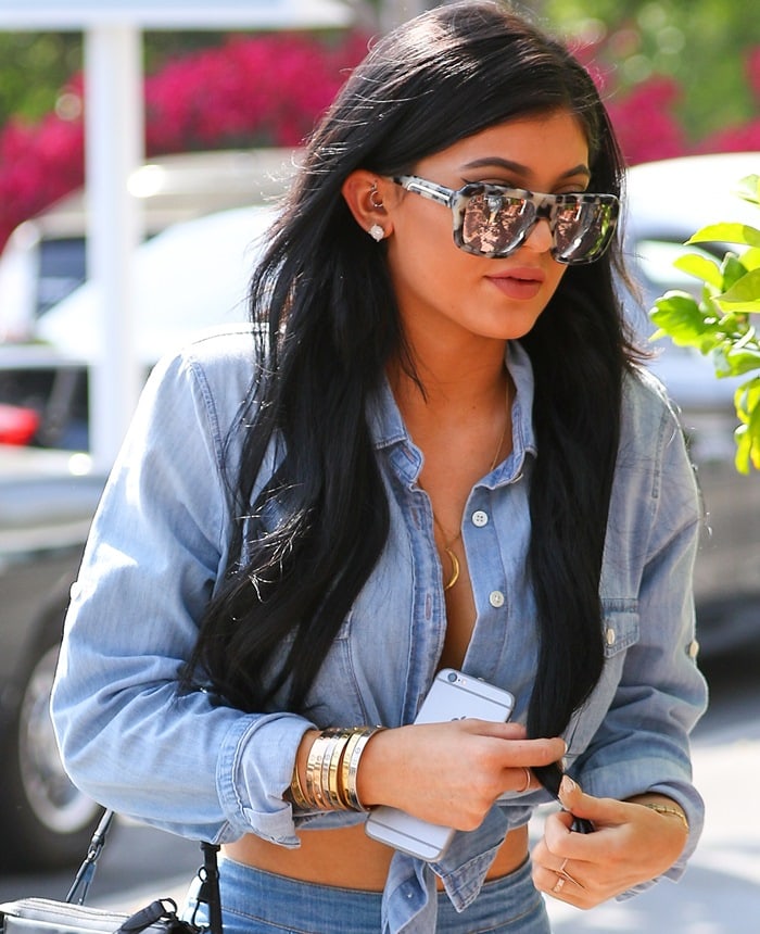 Wearing a double-denim outfit, Kylie Jenner is seen with her phone and a collection of gold bracelets