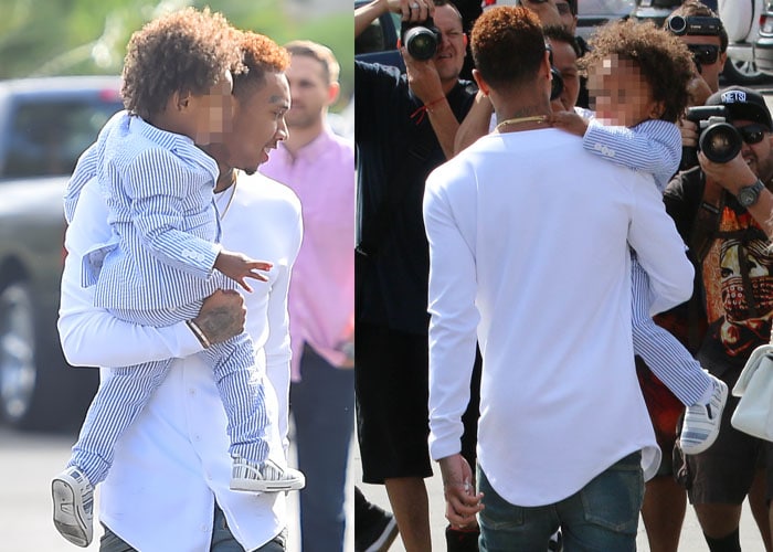 Tyga carries his son, King Cairo, in a matching blue-and-white striped outfit while navigating through a crowd of paparazzi after Easter Sunday service