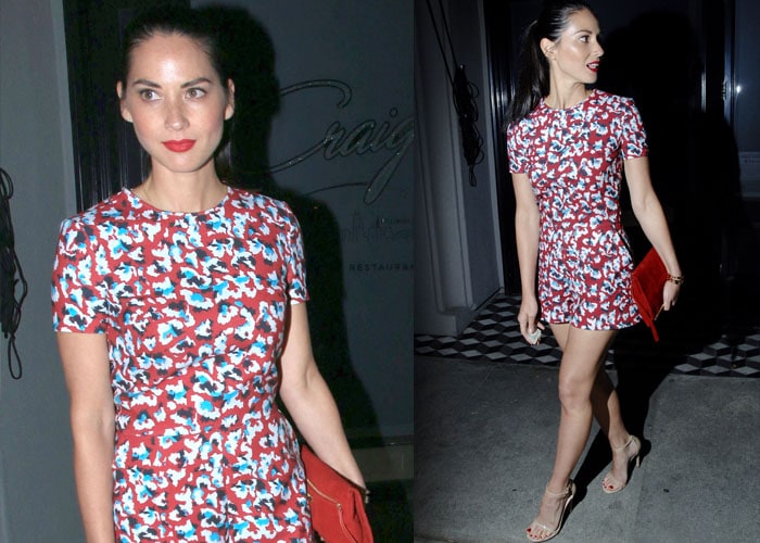 Olivia Munn dazzles in a bold floral romper paired with nude Stuart Weitzman 'Nudist' sandals and a striking red clutch