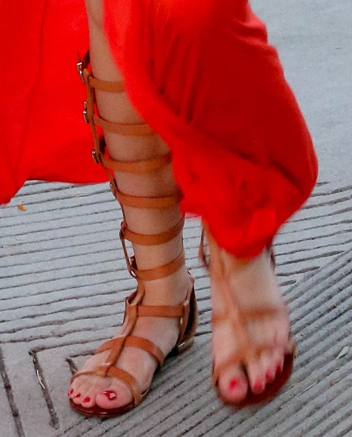 Bella Thorne shows off her pedicure and effortlessly chic style in tan Schutz gladiator sandals, perfectly paired with her vibrant red maxi skirt
