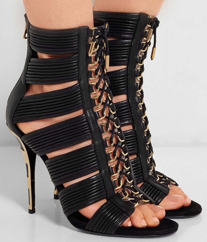 Balmain’s signature cage heels crafted in glossy black leather with gold hardware, featuring ribbed straps, front lace-up detailing, and a sculptural stiletto heel
