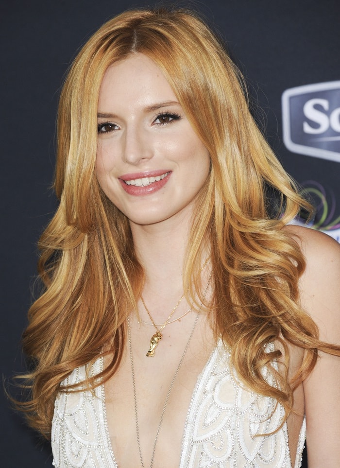 Bella Thorne glows on the black carpet with soft waves and a plunging embellished neckline, adding a delicate gold pendant for a subtle touch of shine