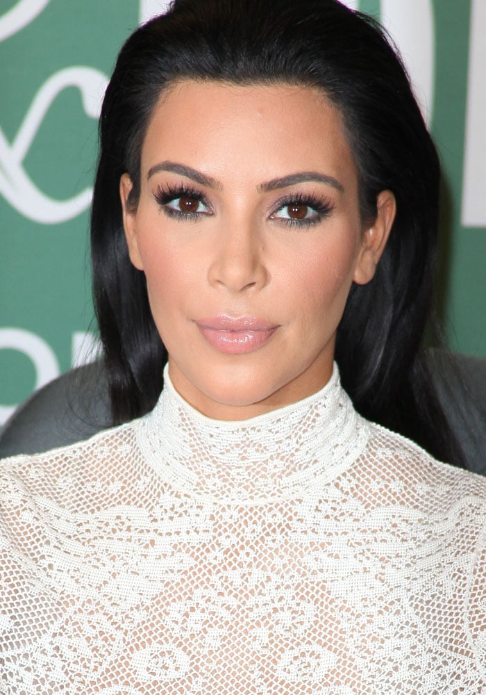 A close-up of Kim Kardashian’s polished beauty look—glossy nude lips, dramatic lashes, and slicked-back hair