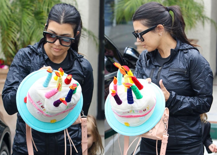 Kourtney Kardashian carries a playful “Happy Birthday” cake decoration