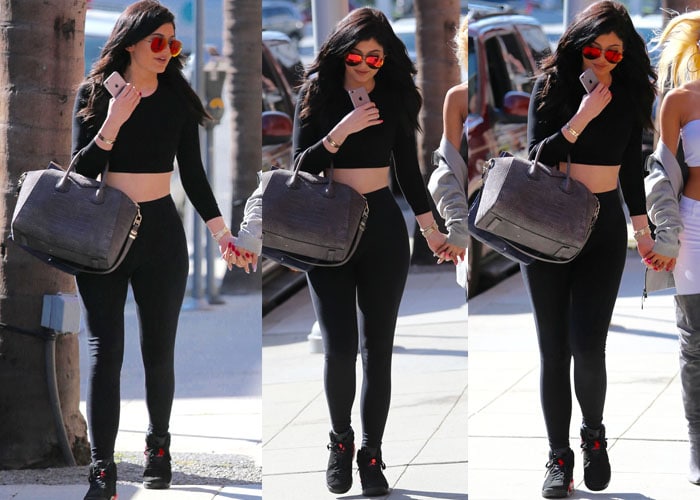 Kylie Jenner pairs a sleek American Apparel stretch crop top and high-waist leggings with Nike Air Jordan 6 Retro sneakers in Black/Infrared 23, Victoria Beckham Classic Victoria sunglasses, an Audemars Piguet Royal Oak watch, and a Givenchy croc-embossed Antigona duffel for a polished, street-luxury look