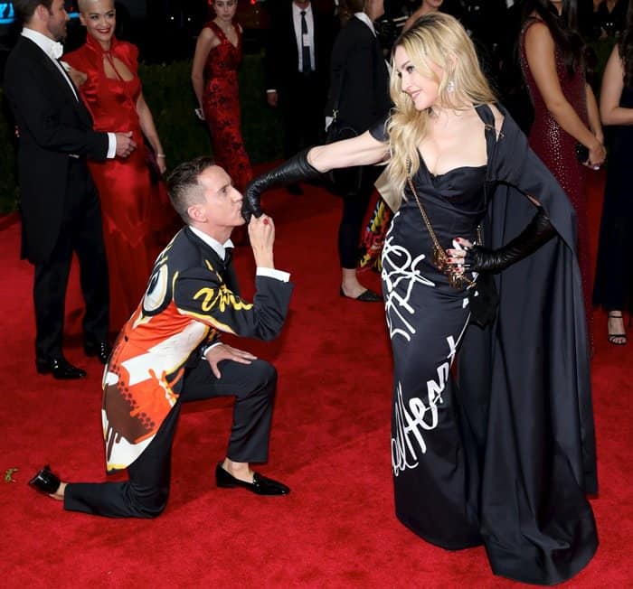 Madonna shares a playful moment with designer Jeremy Scott as he kneels and kisses her hand while she stuns in a custom Moschino gown and matching cape at the 2015 Met Gala