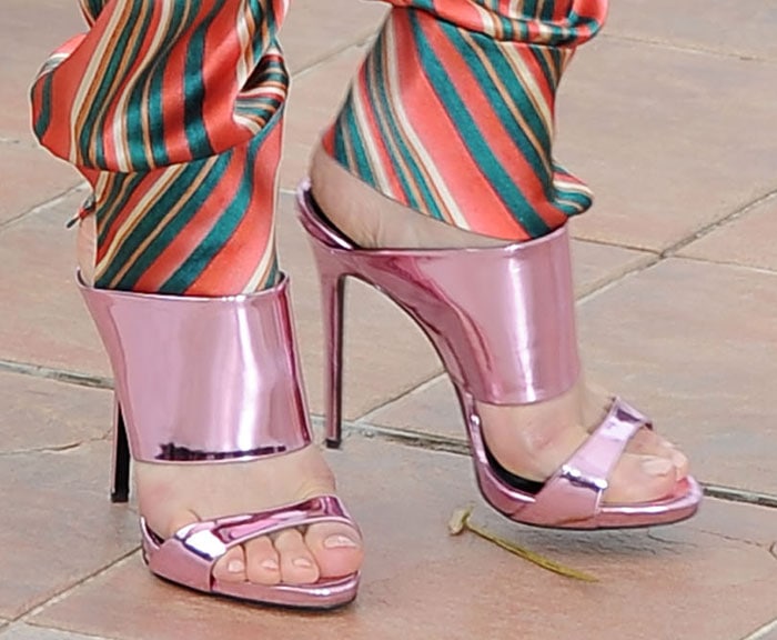 Marion Cotillard's perfectly manicured toes, complementing her metallic pink Giuseppe Zanotti mules, which boldly echo the vibrant, playful hues of her striped Ulyana Sergeenko jumpsuit