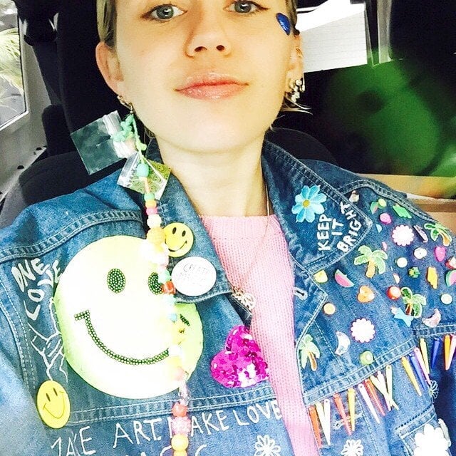 Miley Cyrus shows off her vibrant, decorated denim jacket featuring smiley faces, colorful beads, and playful "Keep It Bright" patches