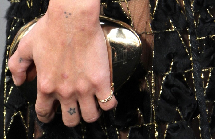 Zoë Kravitz shows off her minimalist gold rings and tiny star tattoo on her right middle finger as she clutches a metallic evening bag