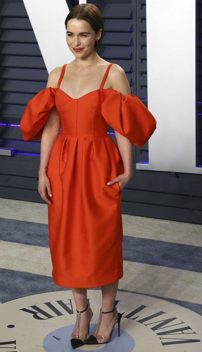 Emilia Clarke in a red Rosie Assoulin Fall 2019 dress with Christian Louboutin shoes, a Tyler Ellis clutch, Nak Armstrong earrings, and an Eriness Jewelry ring at the 2019 Vanity Fair Oscar Party