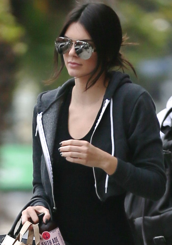 Kendall Jenner rocks a laid-back, sporty look with oversized reflective sunglasses, a black zip-up hoodie, and a bottle of kombucha in hand