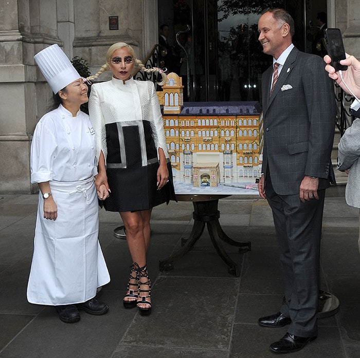 Lady Gaga posing with a very detailed custom cake in celebration of the 150th anniversary of London’s first grand hotel