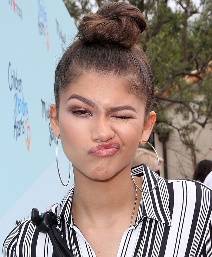 Zendaya added playful charm to her polished look with a cheeky wink, showcasing her bronzy makeup, bold brows, and signature topknot