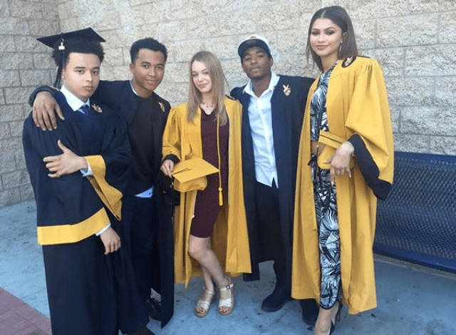 Zendaya stands with her peers and fellow graduates in their caps and gowns on her high school graduation day, visibly sporting her signature red-soled So Kate pumps