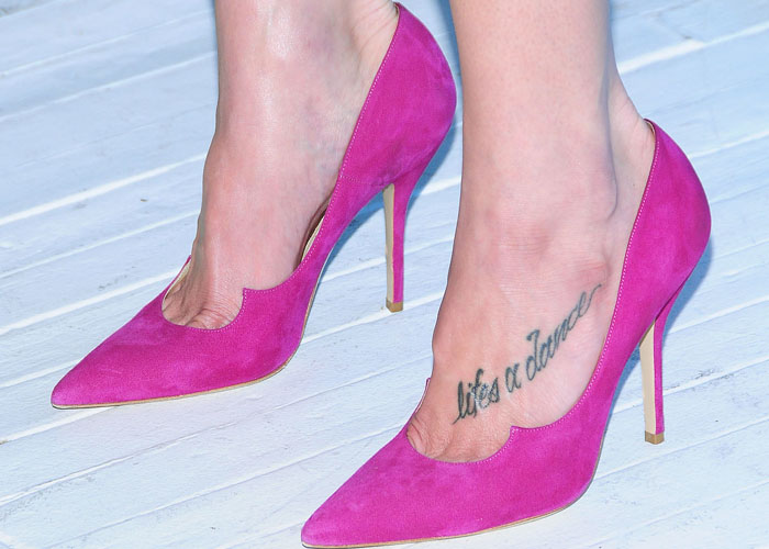 Close-up of Ashley Greene's feet showcases vibrant fuchsia suede Paul Andrew pumps, with a visible "life's a dance" tattoo adorning her foot