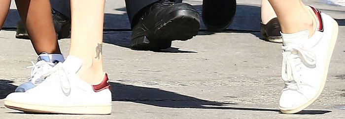 A close-up shot focuses on Charlize Theron's feet, highlighting her white Isabel Marant Bart sneakers with their distinctive red heel detail