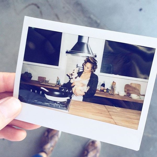 Chrissy Teigen shares a cozy moment in the kitchen, holding her adorable pup while preparing to cook, captured in this candid Polaroid