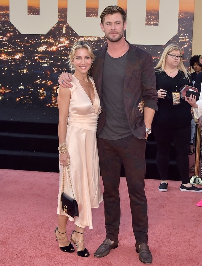 Elsa Pataky embraced effortless bohemian glamour in a flowing ivory Bash “Bernie” dress styled with layered gold jewelry and black-and-gold ankle-strap heels, while Chris Hemsworth complemented her relaxed aesthetic in a subtly patterned Etro suit, open-collar shirt, and dark leather Tod’s loafers at the Los Angeles premiere of Once Upon a Time... in Hollywood on July 22, 2019