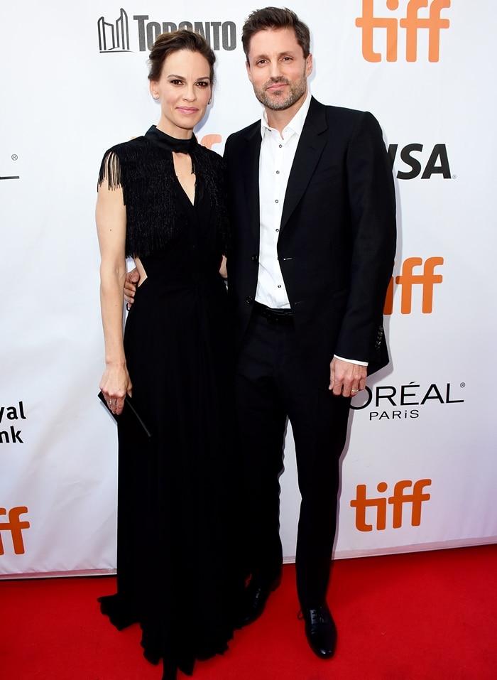 Hilary Swank exuded elegance in a fringed black gown with cutout detailing and peep-toe heels as she posed alongside husband Philip Schneider at TIFF 2018