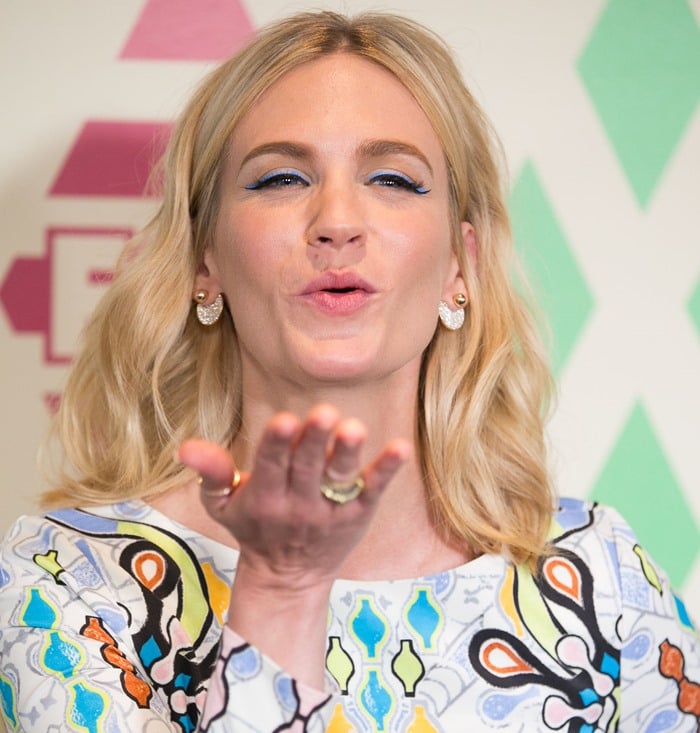 January Jones blows a kiss, showing off her bold blue cat-eye makeup and the playful, board game–inspired print of her Peter Pilotto mini dress