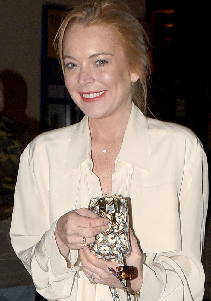 Lindsay Lohan keeps it effortlessly chic in a loose cream blouse and floral clutch while arriving for dinner at Chiltern Firehouse in London on August 11, 2015