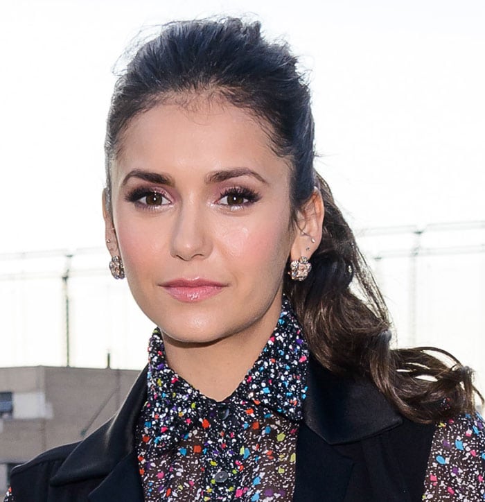 Nina Dobrev keeps her beauty look soft and polished, pairing glowing makeup with sparkling stud earrings and a sleek ponytail