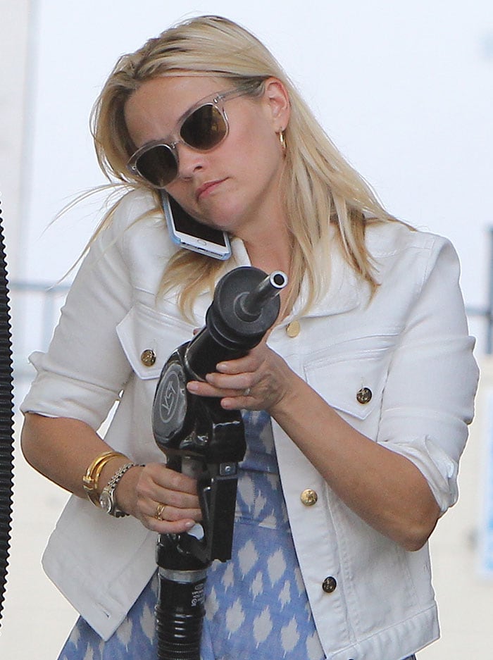 Reese Witherspoon multitasks at the gas pump, balancing her phone call with a chic look in a white denim jacket