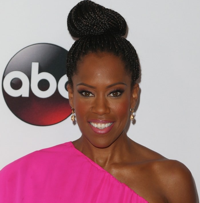 Regina King completed her vibrant ensemble with a sculptural braided updo, soft pink lipstick, and delicate drop earrings