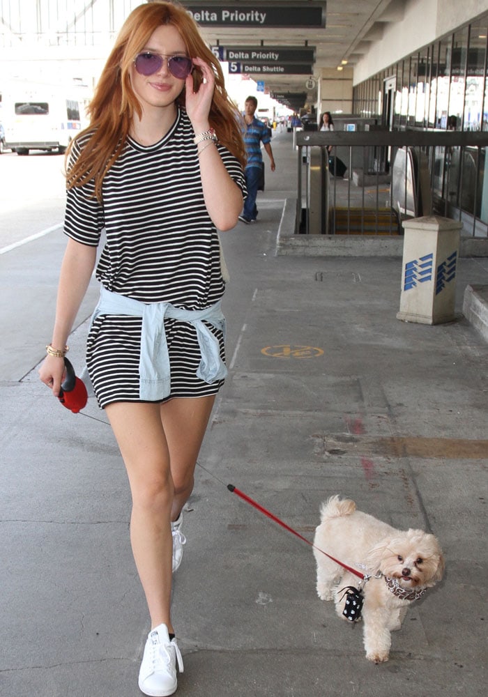 Bella Thorne heads toward the terminal with her dog in tow, pairing a striped tee dress and aviator sunglasses with sleek Stan Smith sneakers