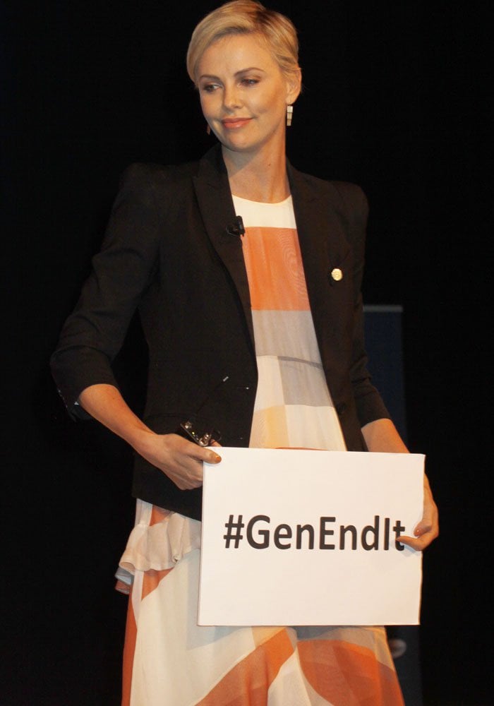Onstage, Charlize underscores her advocacy work by holding a #GenEndIt sign during her Social Good Summit appearance