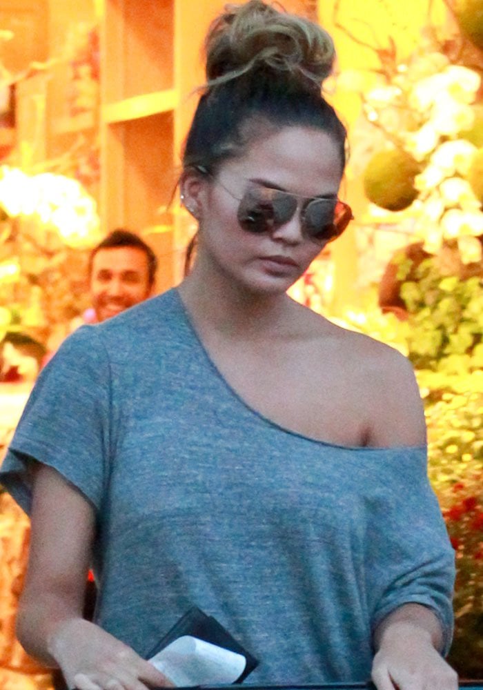 Chrissy Teigen keeps her grocery-run look effortless with mirrored aviators, a messy top knot, and an oversized off-the-shoulder R13 tee