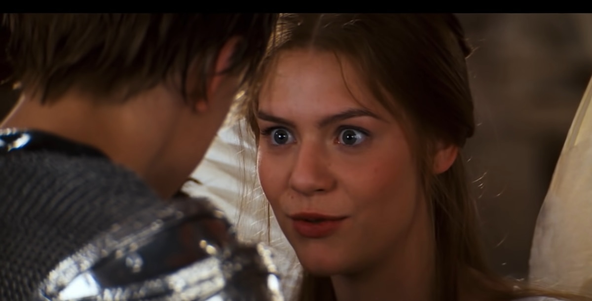 Claire Danes, dressed as Juliet in an ethereal white angel dress with delicate wings, shares an intense moment with Leonardo DiCaprio’s Romeo in Romeo + Juliet