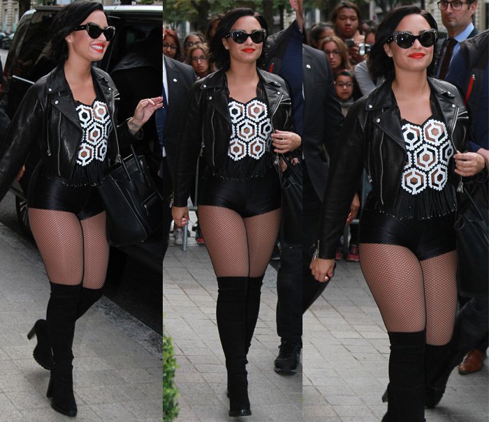 Demi Lovato turns up the edgy glamour in Paris, pairing a leather moto jacket with a sheer embellished top, black shorts, fishnet tights, thigh-high boots, and her signature Celine tote at Le Royal Monceau on September 5, 2015