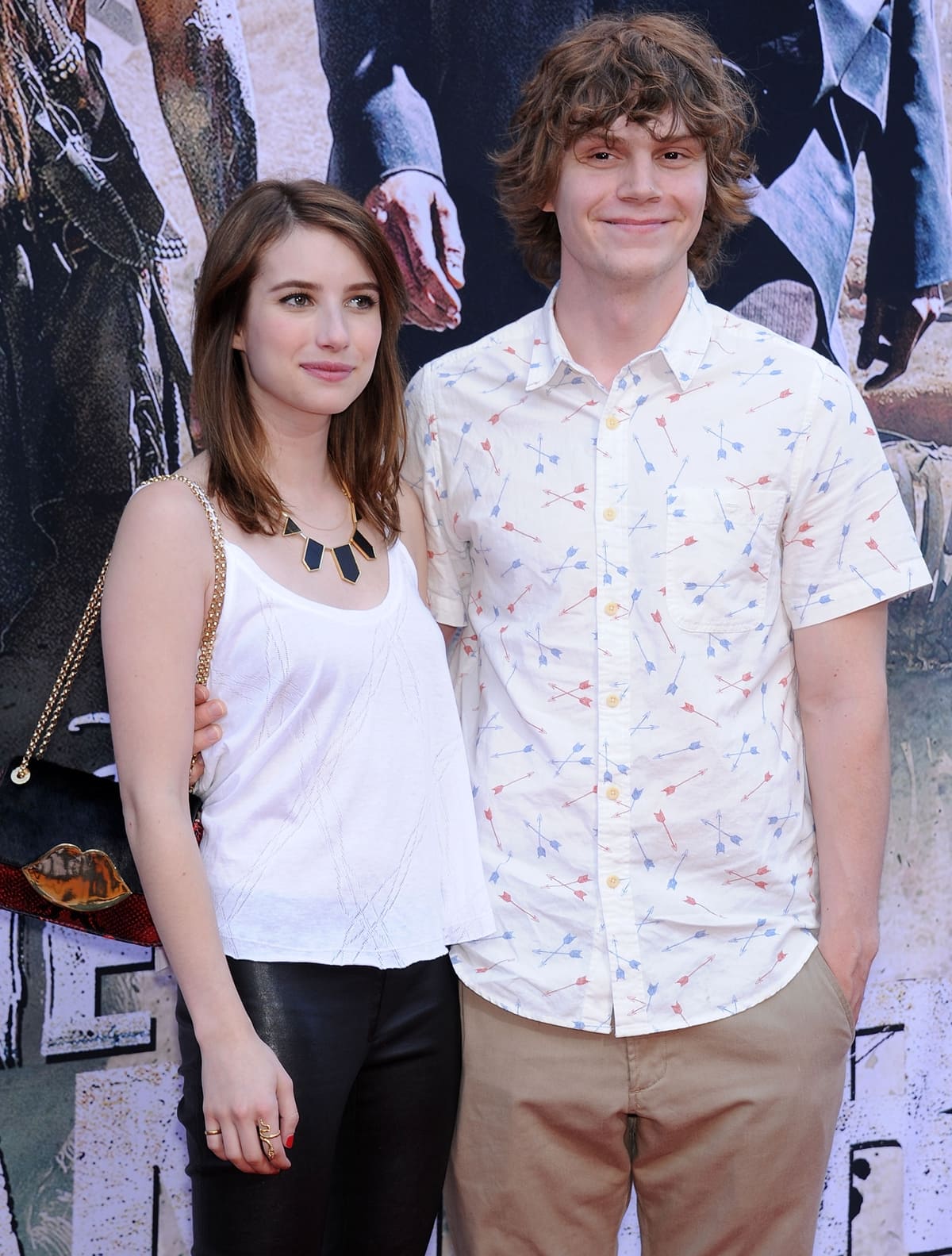 Emma Roberts and Evan Peters attend a red carpet event, with Emma in a chic white tank, black leather pants, and statement necklace while Evan keeps it casual in a printed button-down shirt and khaki trousers