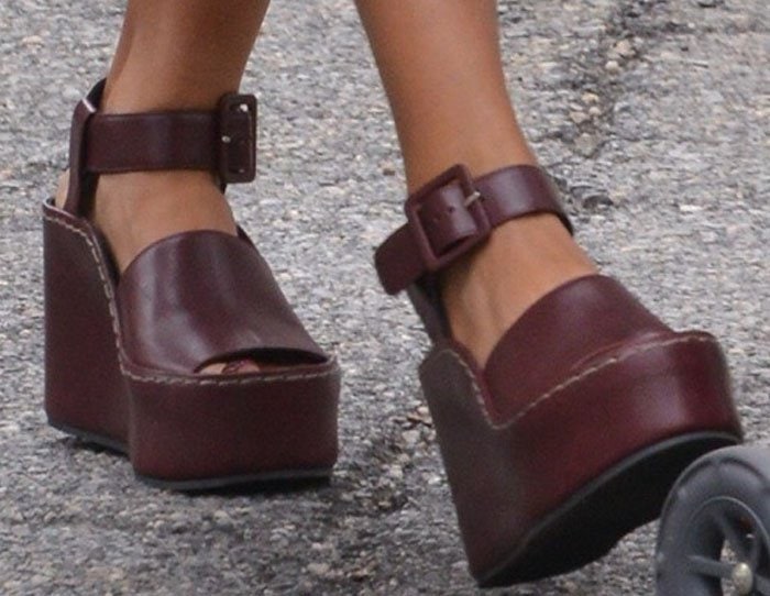 Jessica Alba’s burgundy Céline wedges feature oversized ankle straps, dramatic wooden platforms, and a sharply carved geometric heel