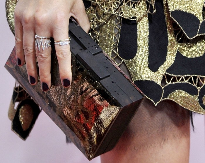 She finishes the look with a structured black Rauwolf clutch, her deep plum manicure and stacked rings adding a sharp, modern contrast to the intricate gold embroidery