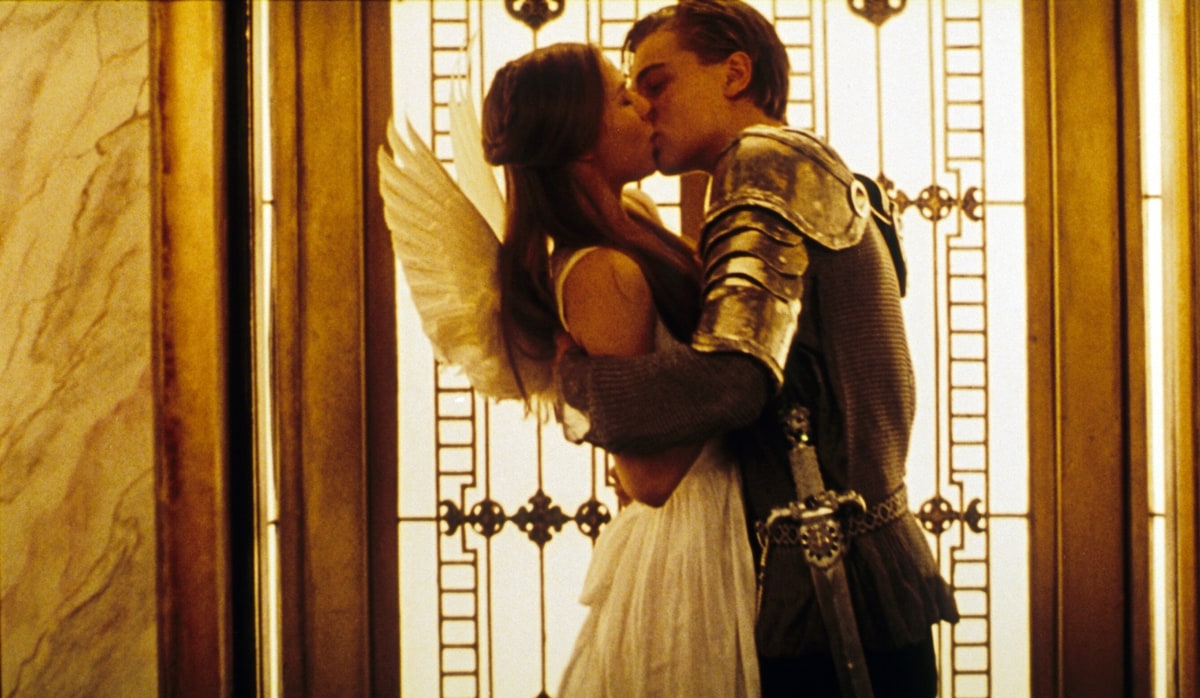 Claire Danes, dressed as an angel in a white dress, shares an iconic kiss with Leonardo DiCaprio in a knight’s armor during the masquerade ball scene in Romeo + Juliet (1996)